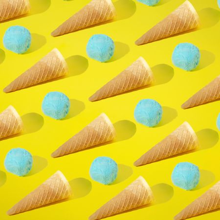 Rows of blue ice cream scoops and cones on yellow background