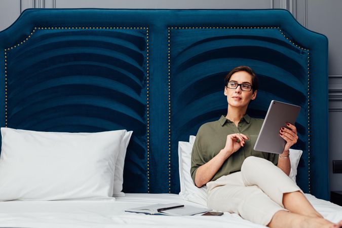 Woman sitting on a bed with a blue headboard working on a tablet
