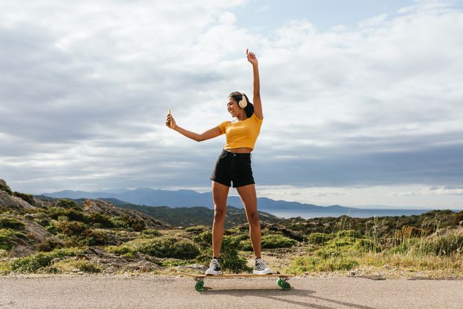 Smiling woman on longboard raising hand and taking selfie