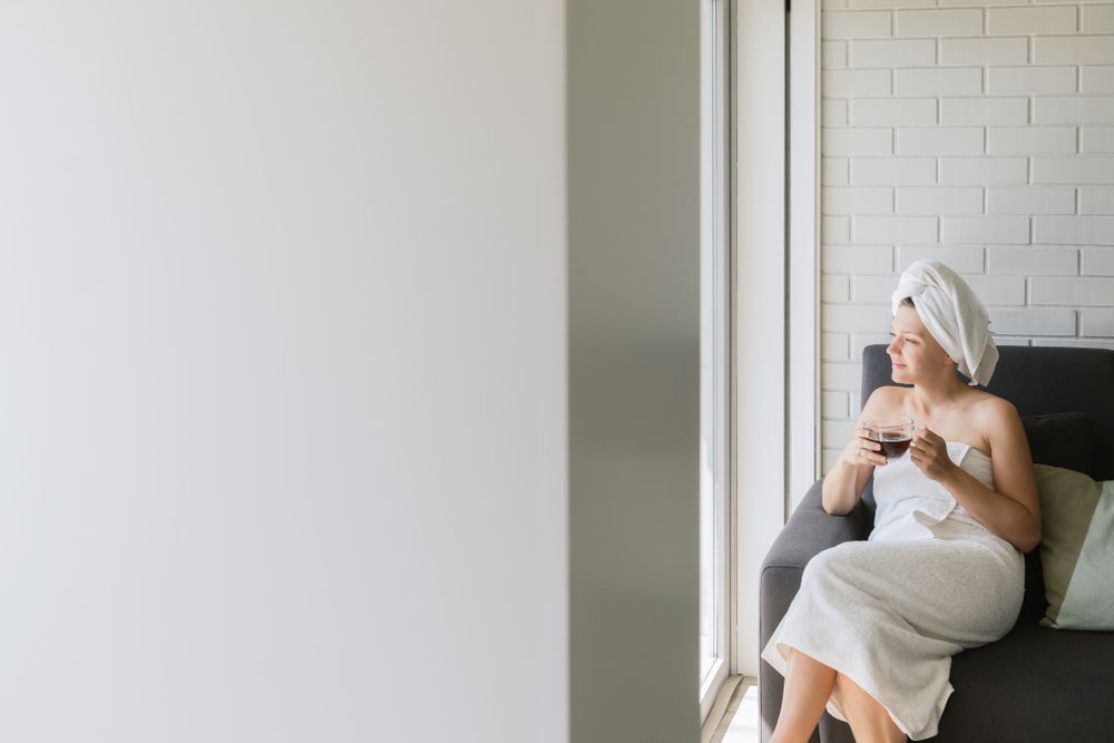 Adult relaxed woman enjoying life while resting on sofa and having hot drink after shower in own cozy apartment