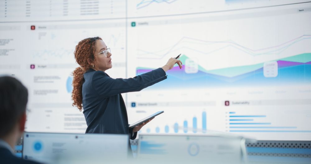 Data Scientist Reviewing Reports Of Risk Management Department On Big Digital Screen In Monitoring Room.
