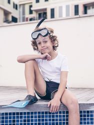 Pensive preteen boy in snorkeling mask and flippers on poolside