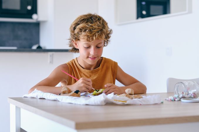 Content preteen boy painting stone at table
