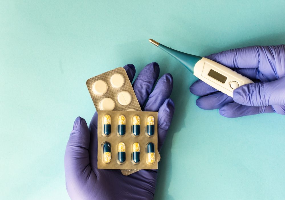 Covid-19 virus concept of looking down at hands in latex gloves with pills and digital thermometer