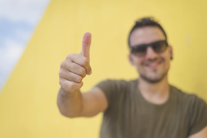 Happy male with thumbs up in front of yellow wall outside