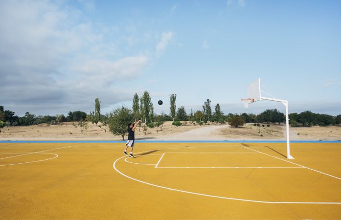 Young man playing on yellow basketball court outdoor.