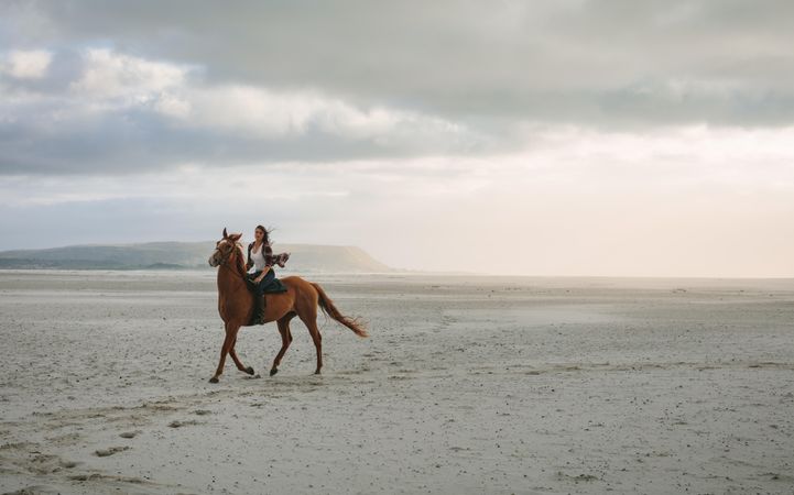 Woman horse riding along the sea shore in evening