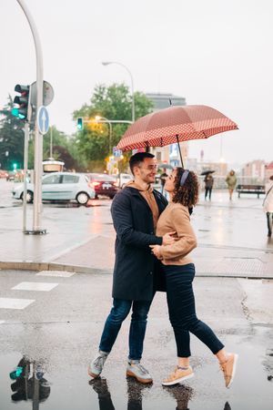 Happy couple with umbrella hugging on wet street