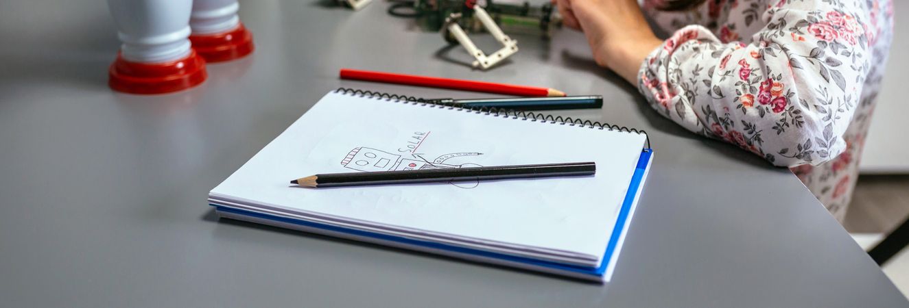 Robot draw by child on notebook and student connecting wire in electrical circuit on background