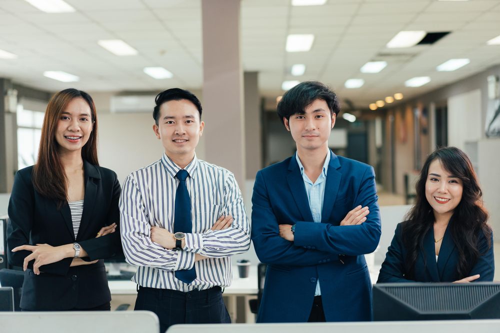 Group of Asian corporate workers with arms crossed looking at camera at their workplace