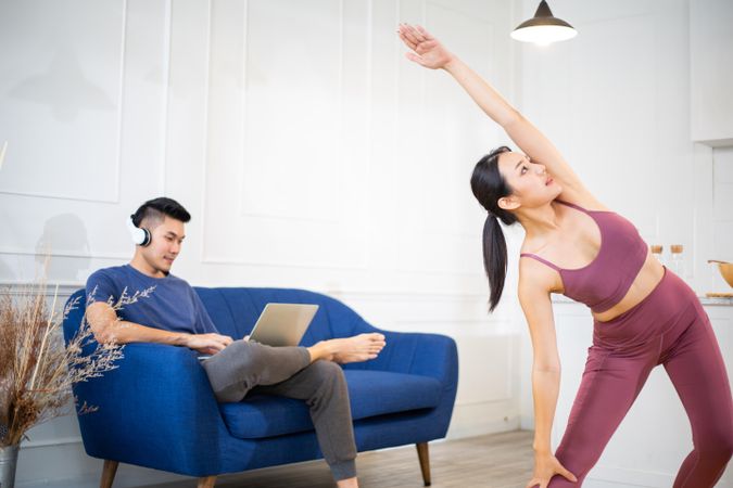 Woman stretching with partner on sofa in the background