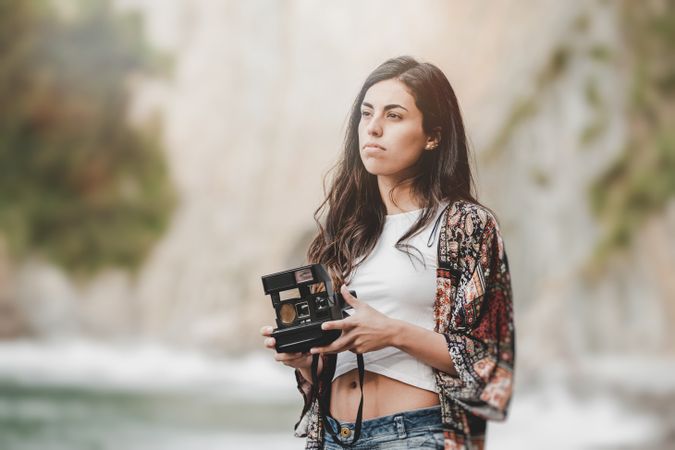 Woman with camera on shore near stones and water