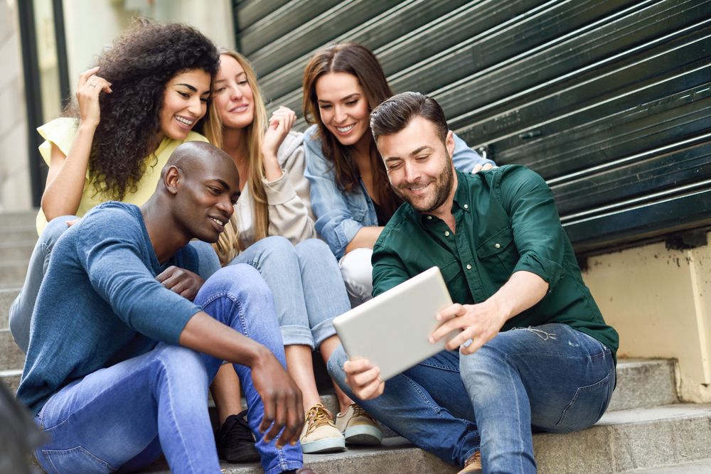 Friends enjoying something on digital tablet while sitting on outdoor cement staircase