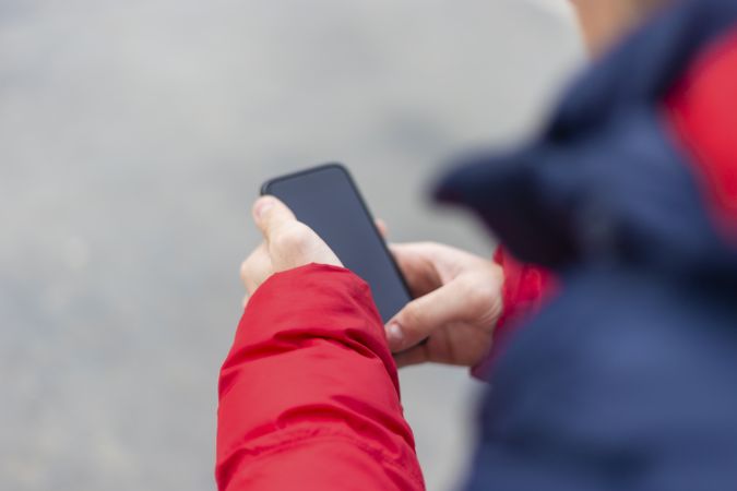 Over the shoulder shot of hands of man with smartphone texting outdoors in the street