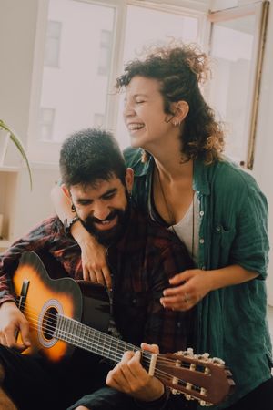 Cheerful couple playing guitar at home