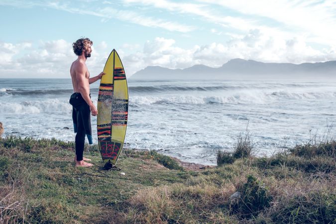 Male surfer with surfboard on coast of waving sea