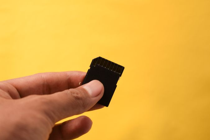 Hand holding SD card on yellow background