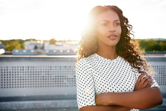 Calm Black woman with arms crossed on sunny rooftop looking off into the distance