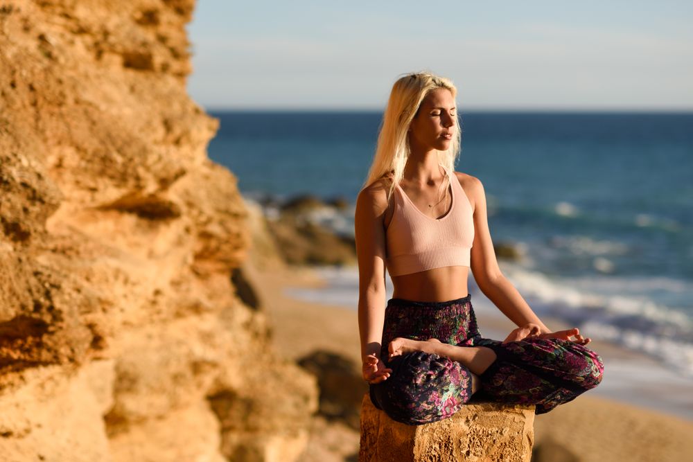Blonde woman meditating on rocks over looking beach