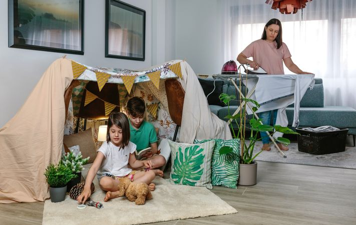 Mother ironing while her children play camping at home