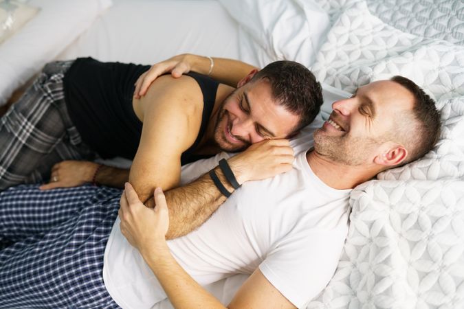 Two males smiling and lying together in bed