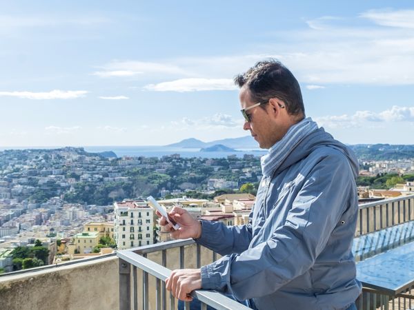 Man wearing sunglasses standing on a terrace while using his smartphone