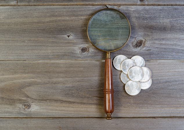 Silver dollar coin collection and old magnify glass on rustic wood