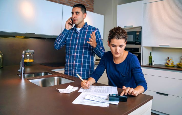 Man on phone as woman works on bills in kitchen counter