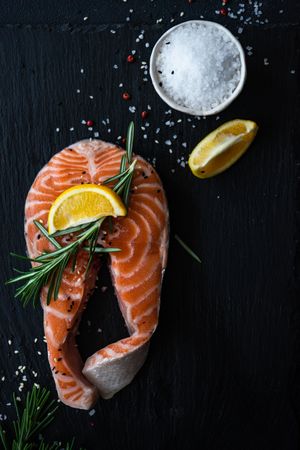 Salmon fish steak with rosemary and lemon on dark counter with copy space