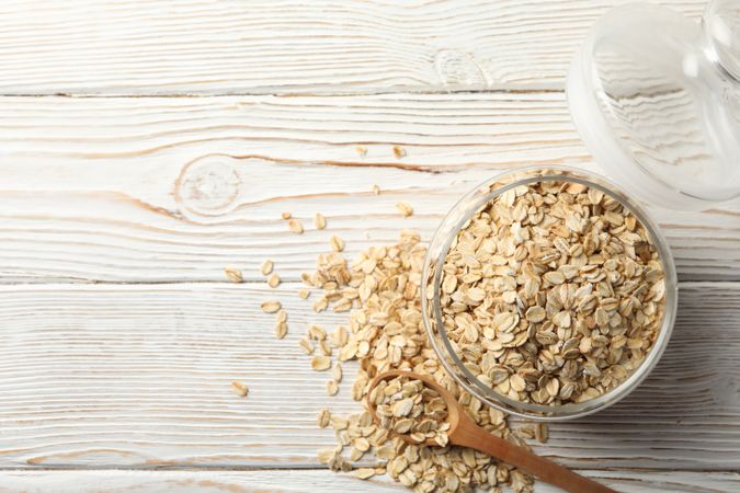 Glass jar with oatmeal and spoon on wooden background, top view