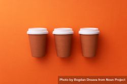 Three disposable coffee cups on orange background bGMzA5