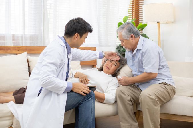 Doctor with hand on forehead of ill older woman