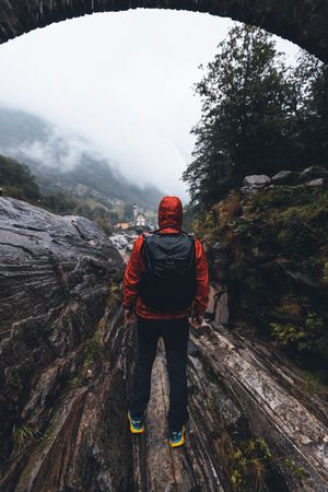 Back view of a man in red jacket with backpack walking under bridge