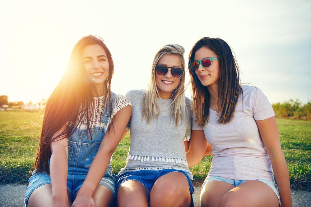 Happy female friends sitting in sunny field with sun flare