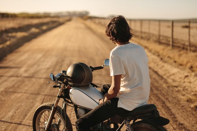 Rear view of young man sitting on his bike and looking at empty country road