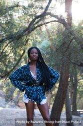 Fashion shot of woman standing in the woods with a flannel shirt smiling at camera 4mWvQ0
