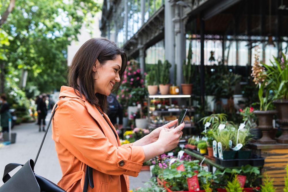 Content woman taking photo of flowers in garden center