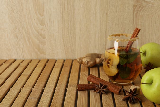 Glass with cider, apples and spices on wooden background, space for text