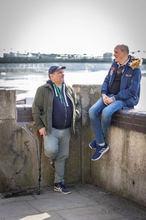 Two older male friends sitting by the river and talking