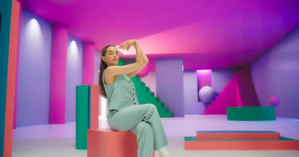 Portrait of Young White Woman Sitting in Geometric Abstract Environment, Dancing with Hypnotic Graceful Movements. Fashionable Female Dancer Practicing Routine in Colorful Studio