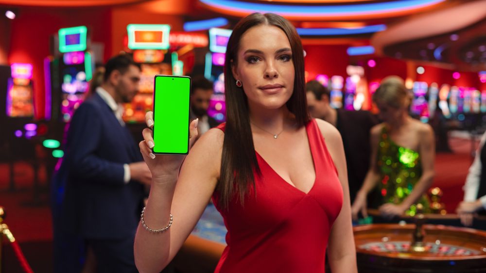 Portrait of a Woman Posing in a Red Dress, Holding a Smartphone with Green Screen Mock Up Display to Use as a Template