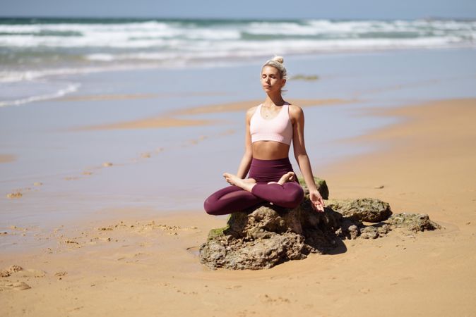 Woman sitting on a rock, meditating on a Spanish beach