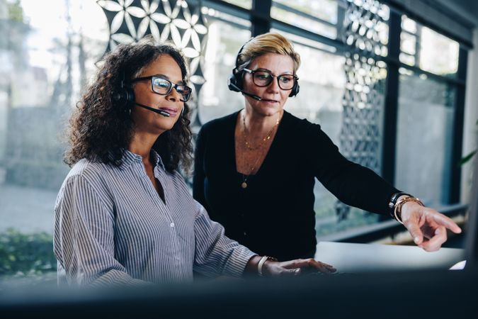 Two businesswomen wearing headsets working together on computer