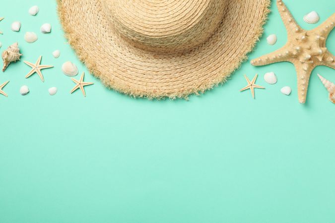 Straw hat and starfishes on mint background, top view