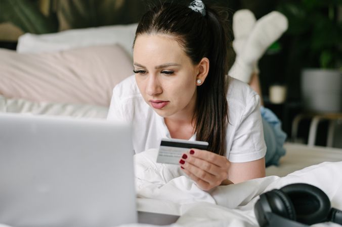 Focused woman with netbook and credit card in bedroom