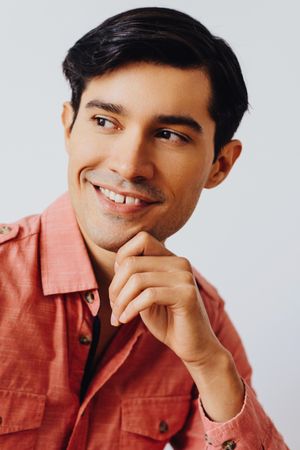Headshot of smiling Hispanic male looking away from camera in grey studio, vertical