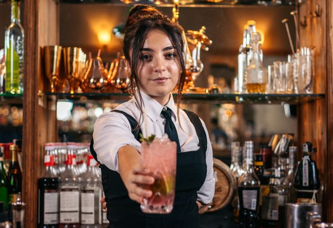 Young female bartender offering a drink