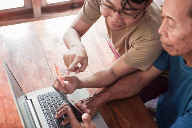 Happy adult son and older father pay online using laptop and credit card