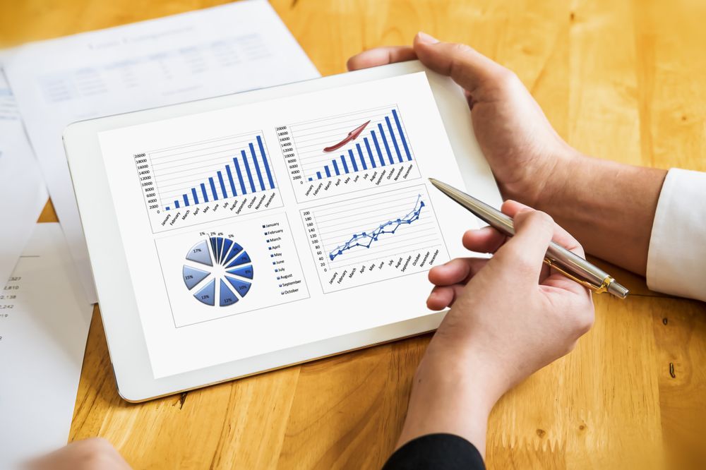Hands Analyzing Business Charts on a Tablet Screen at a Wooden Desk