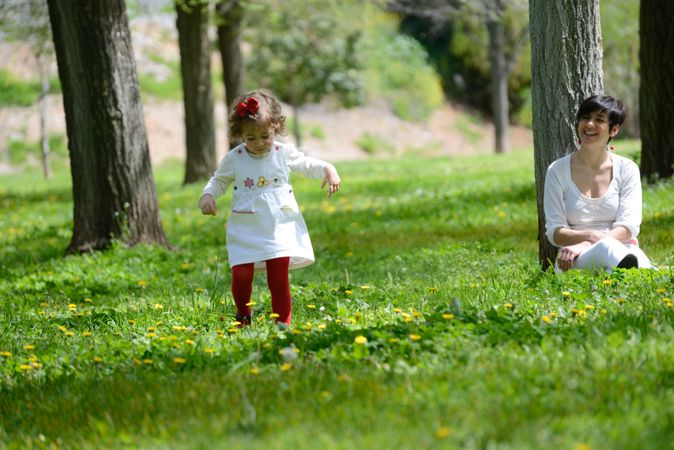 Woman smiling and watching girl walk in sunny park